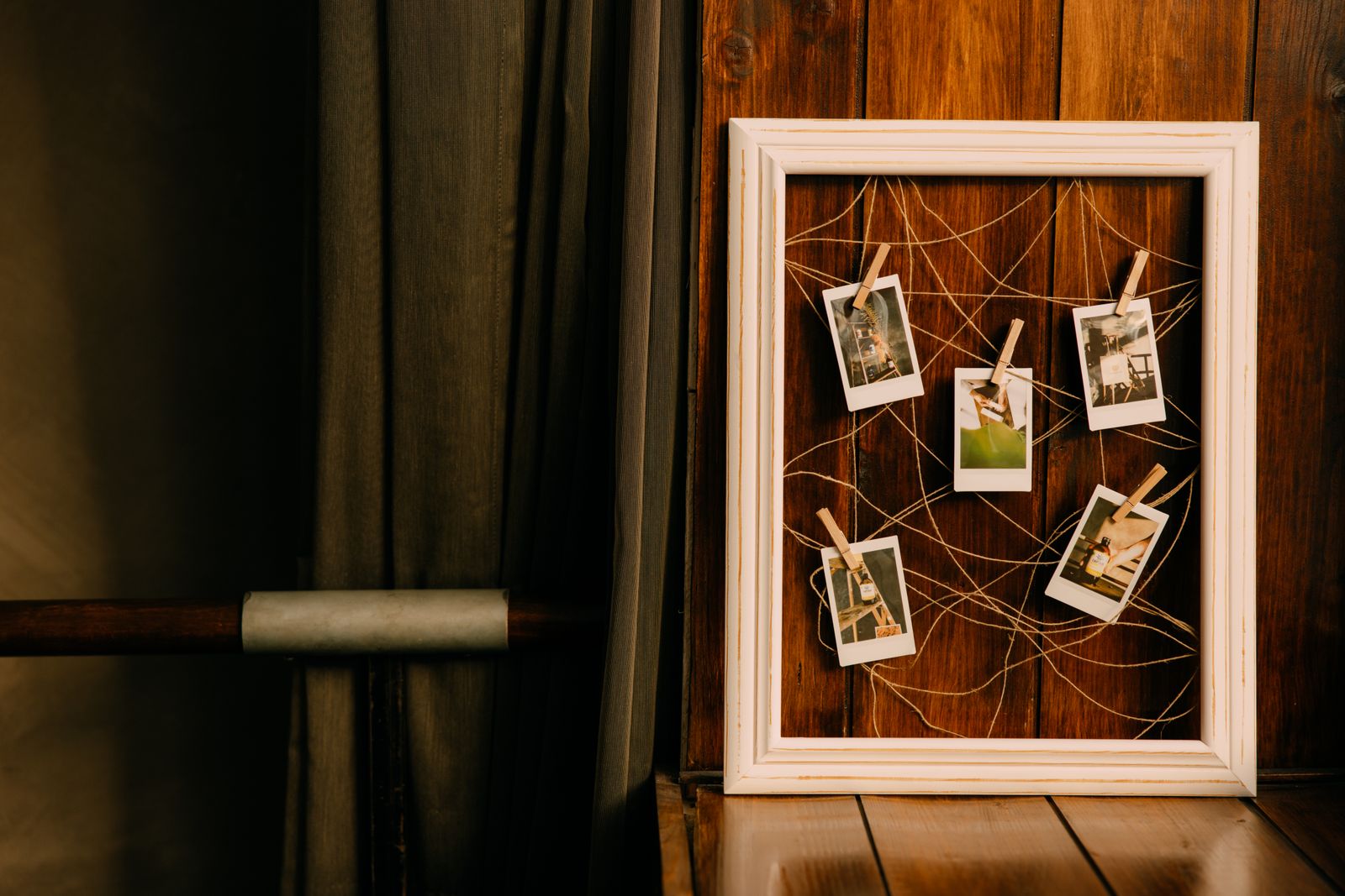 Fotos polaroides emolduradas e presas com barbante dentro de uma moldura de madeira